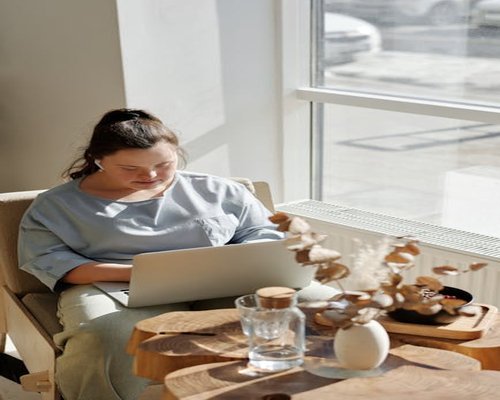 Person relaxing next to a window with warm sunlight illuminating a laptop
