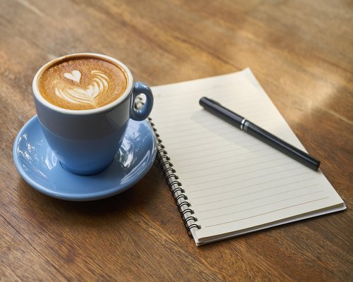 A well lit desk corner near a window with a notebook and coffee cup