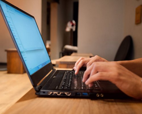 Person typing on a laptop computer positioned comfortably on a wooden desk